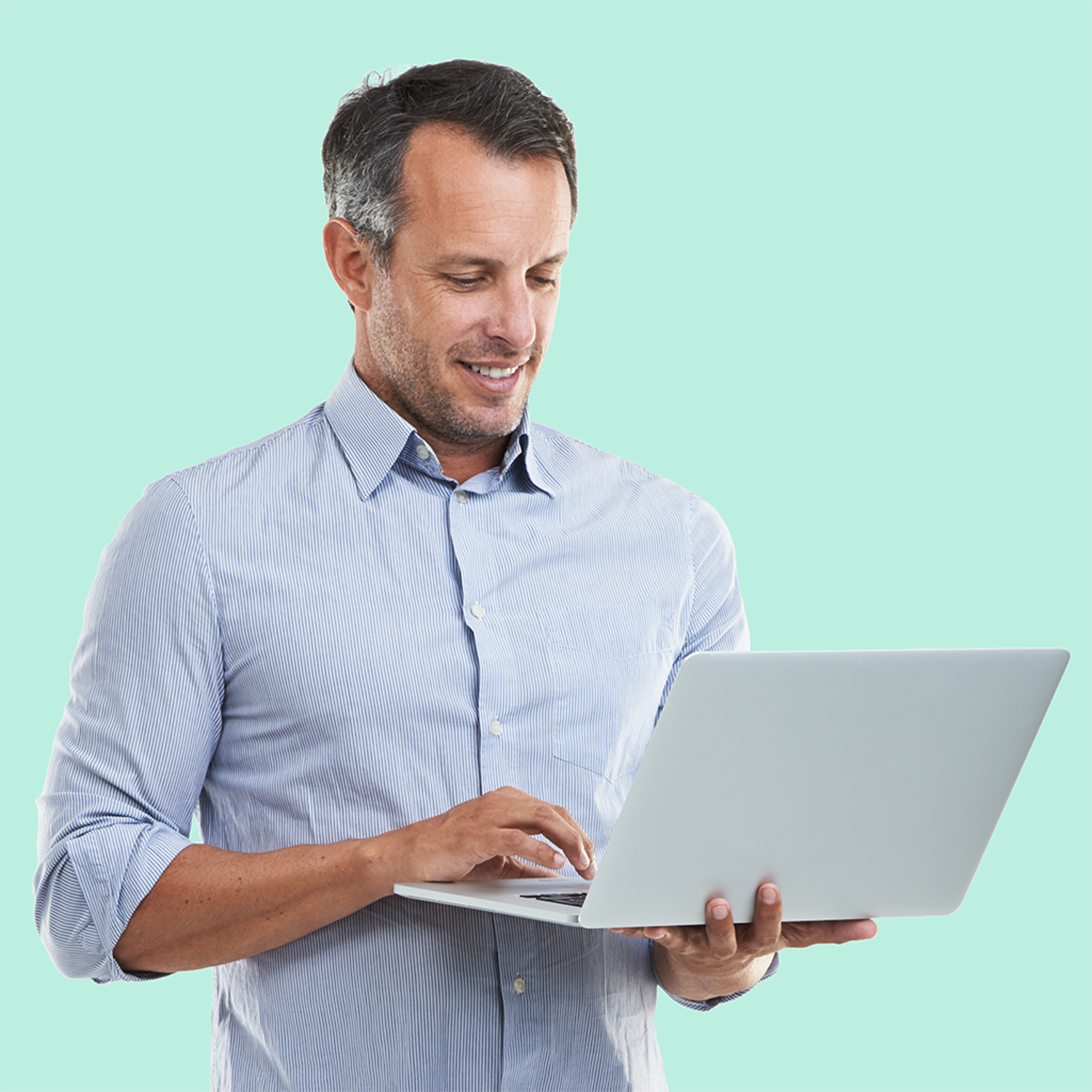 A smiling man with short, graying hair holds an open laptop in his hands. He is wearing a light blue, pinstriped button-down shirt and is looking down at the screen. The background is a solid, light blue-green color.